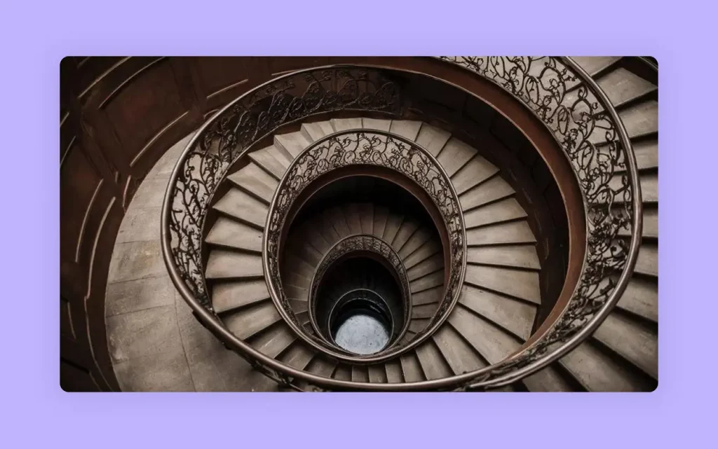 A downward view of a vintage spiral staircase with railings. 