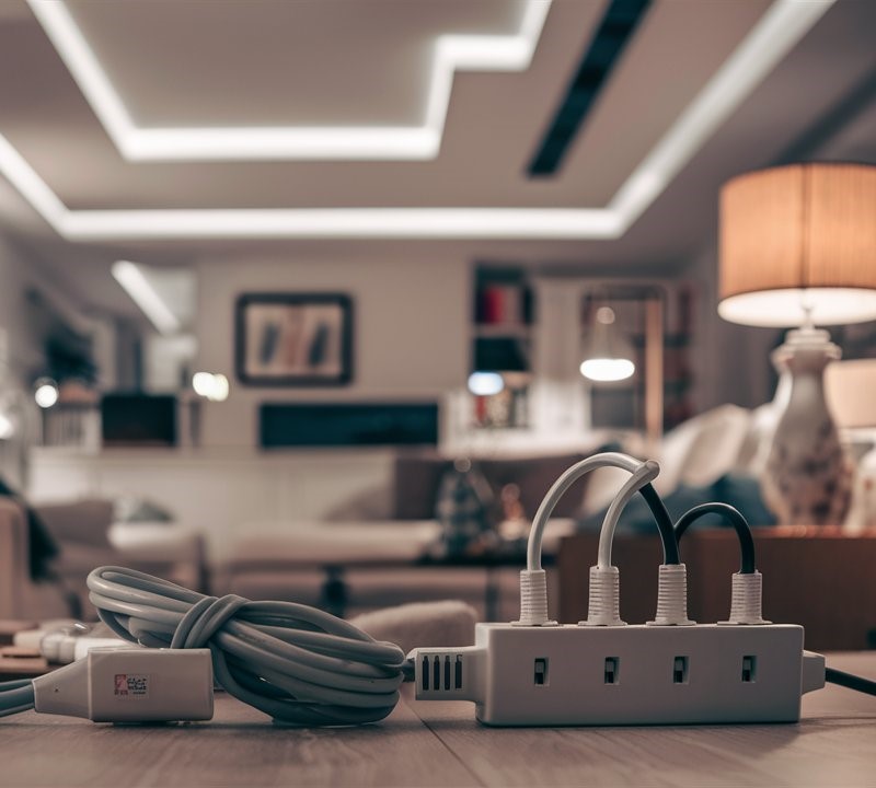 A white power strip with multiple cables plugged in lies on a wooden floor